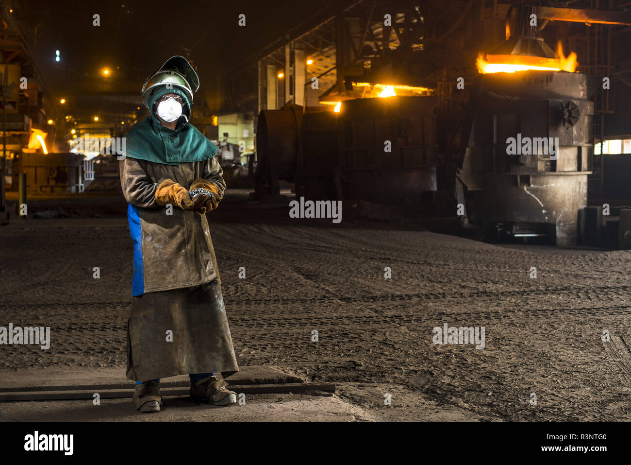 Worker holding ferronickel shot in front of molten furnaces. New