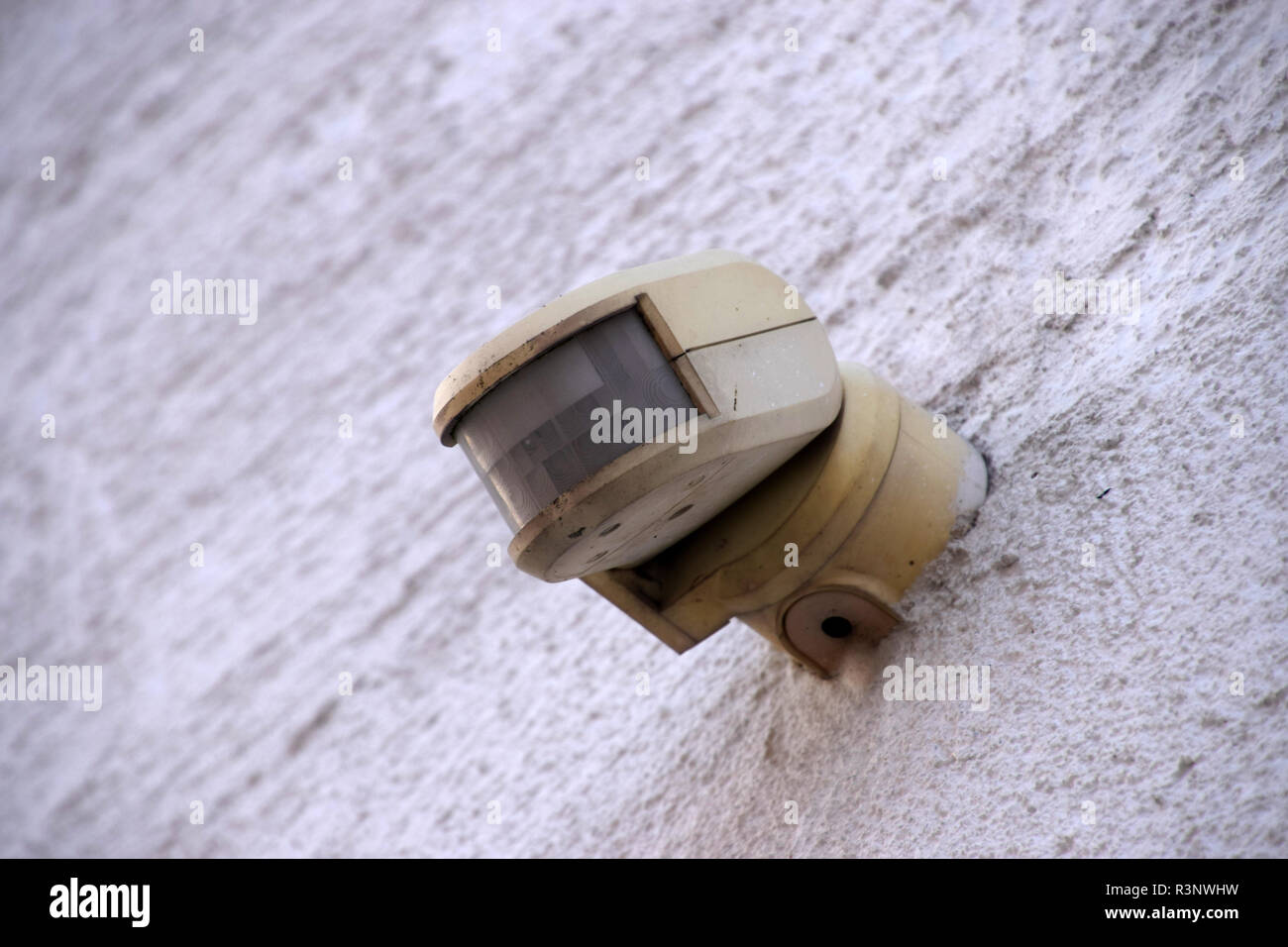 wall motion detector in a simple design, old and dirty motion detector on a house wall in the outdoor area Stock Photo