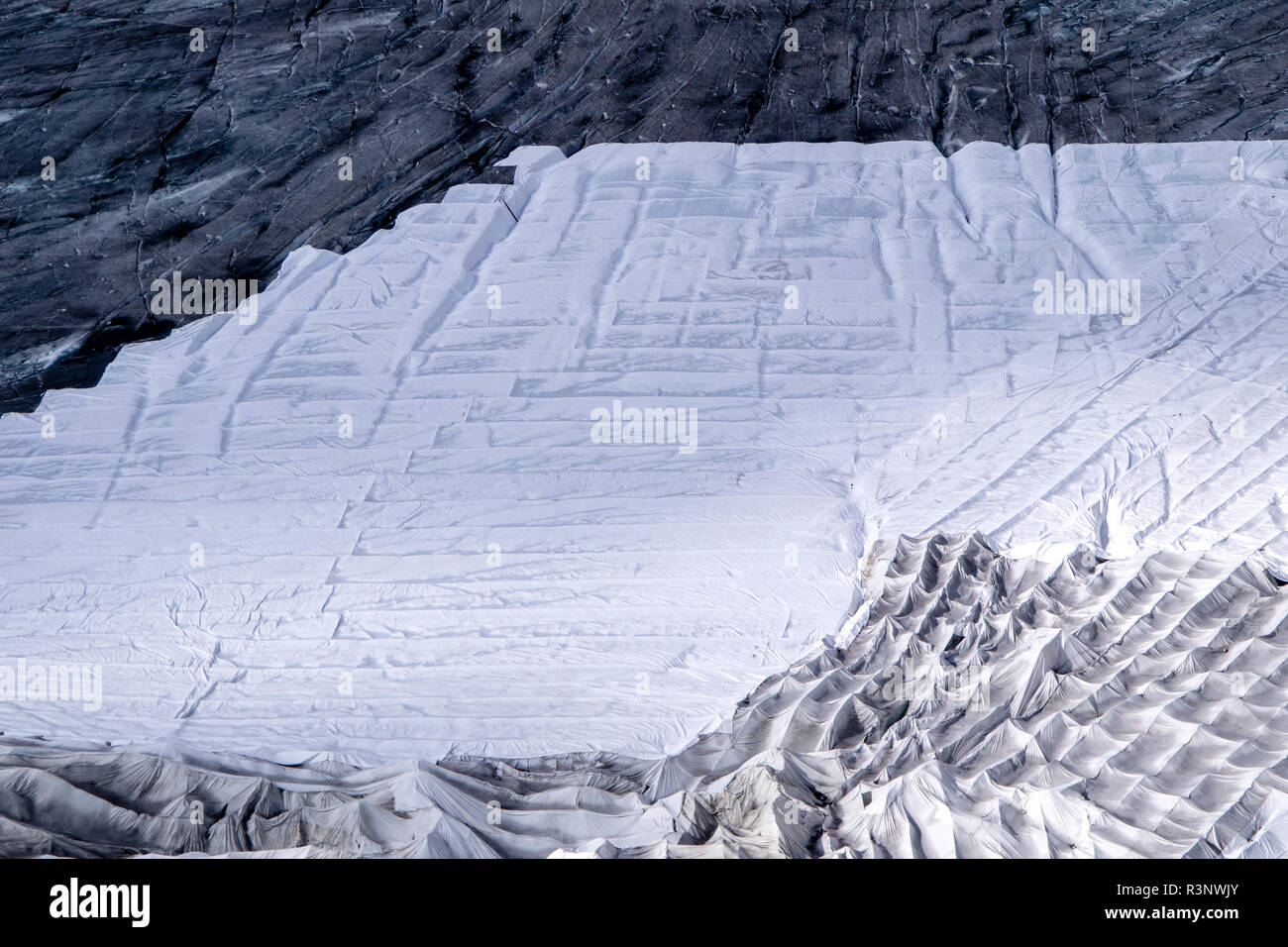 Climate | Albedo | Rhone: Huge fleece blankets cover parts of the Rhone Glacier in Switzerland in an attempt to stall the inevitable melting of the snow and ice. After a winter with record amounts of snow, most of it was gone when this image was taken on July 14th 2018, exposing the darker ice. While snow is a brilliant reflector of the energy from the sun, the darker ice absorbs the energy instead, accelerating the melting of the glacier. The color and darkness of glacier ice vary all over the world, depending on build-up of pollution, age of the ice, particles picked up by the ice and by mic Stock Photo