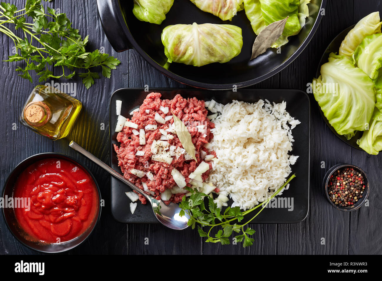 raw stuffed cabbage leaves with ingredients - minced beef, boiled rice, parsley and tomato sauce on a black table, view from above, flat lay,, close-u Stock Photo