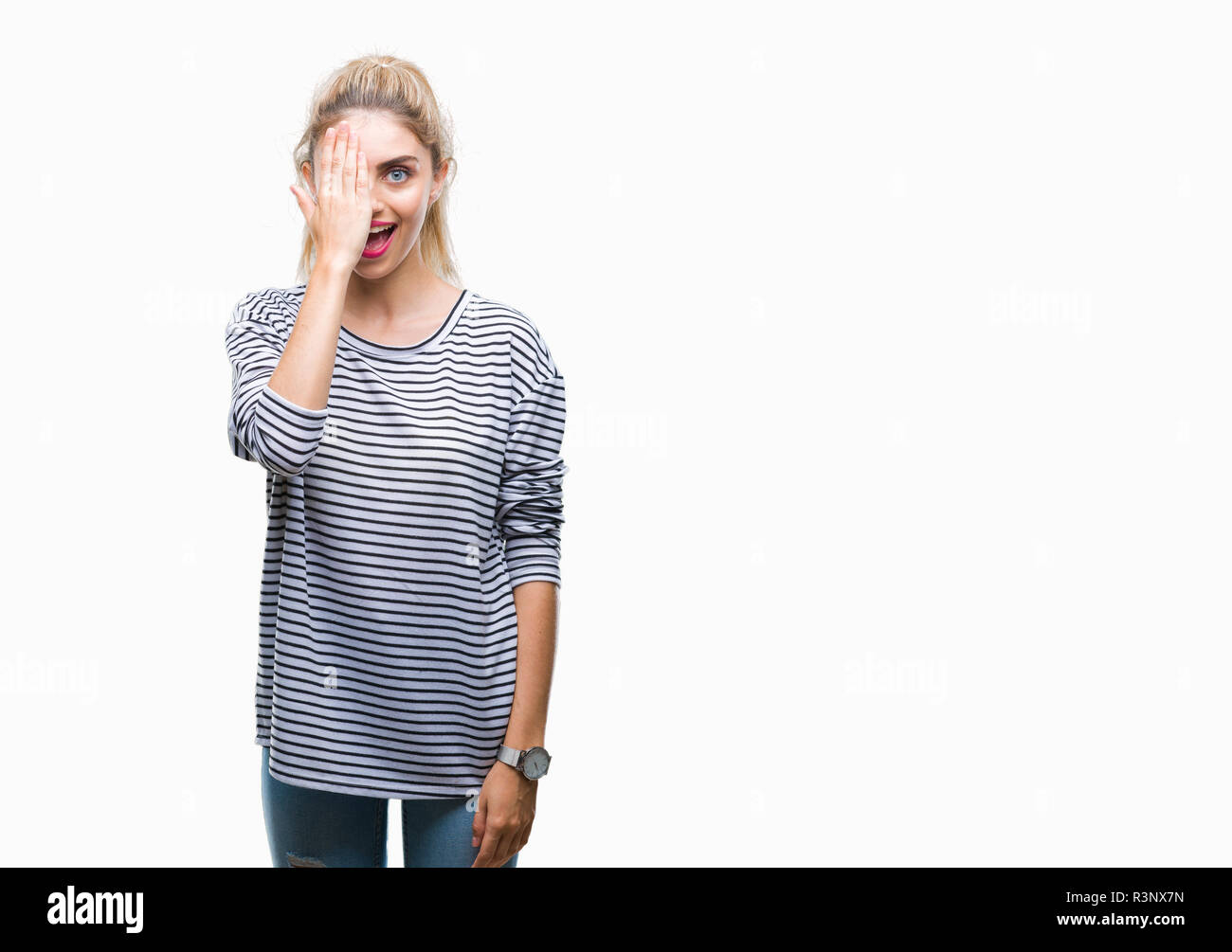 Young beautiful blonde woman wearing stripes sweater over isolated background covering one eye with hand with confident smile on face and surprise emo Stock Photo