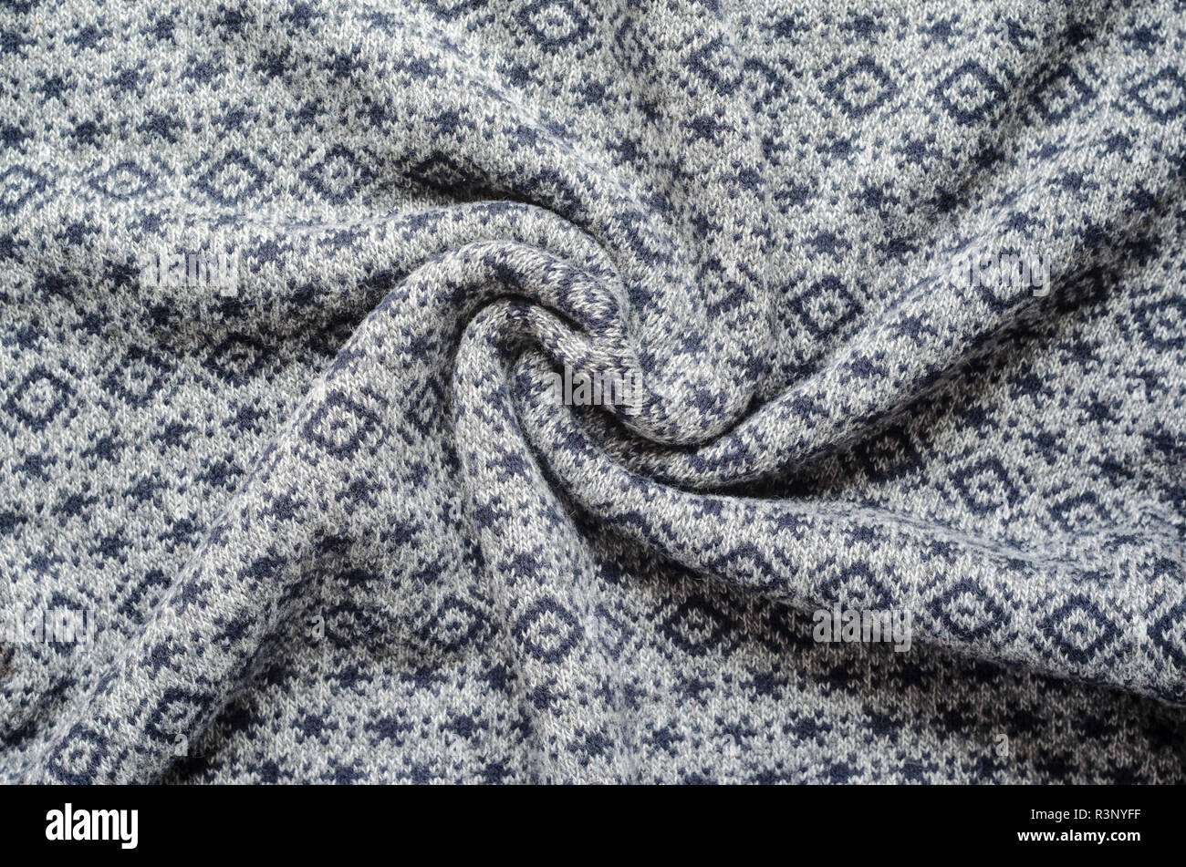 Crumpled background of gray winter sweaters with repeating geometric patterns and small snowflakes. Twisted in the center knitted fabric swatch Stock Photo