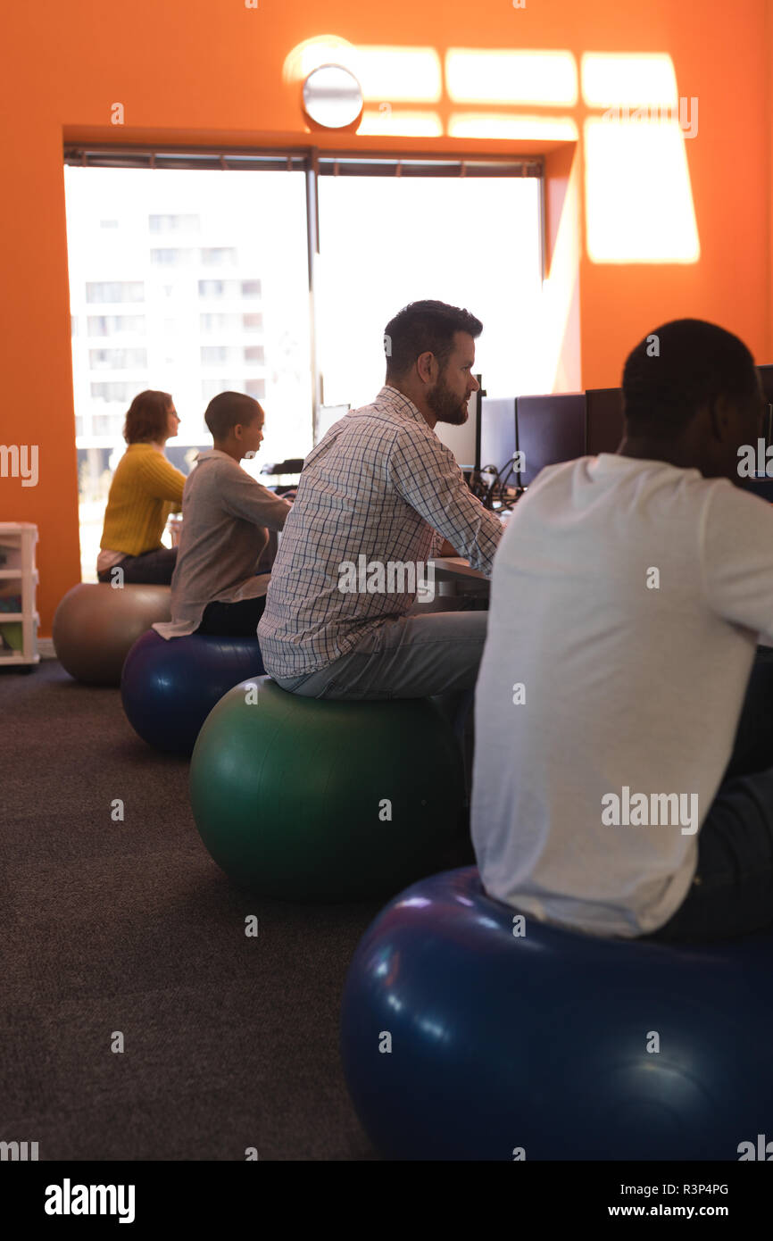 Business Executives Working At Desk While Sitting On Exercise Ball
