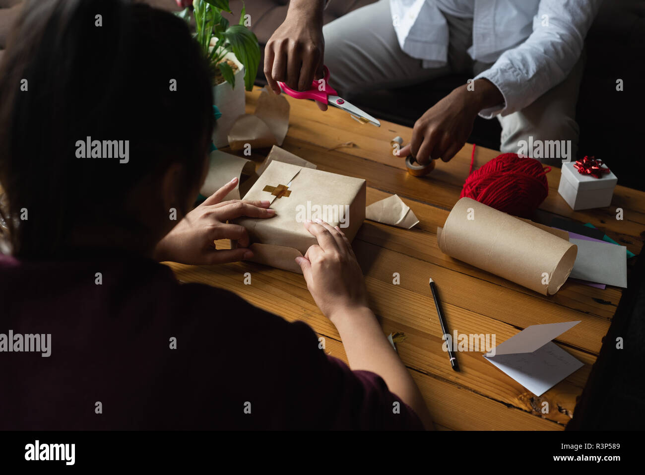 Couple wrapping gift box in living room Stock Photo