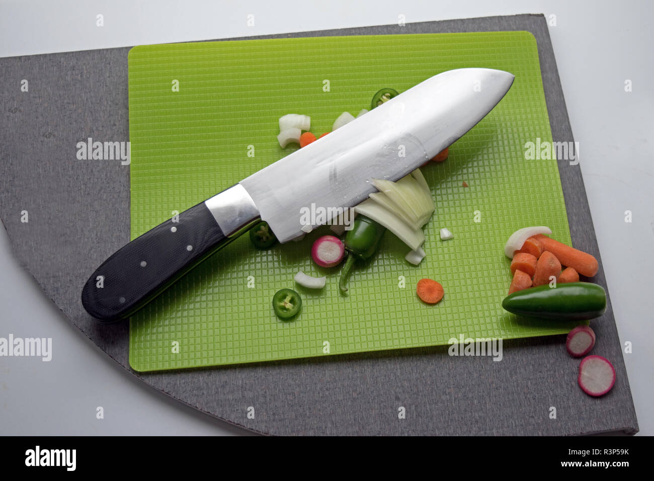 A big knife is used to cut up vegetables on a green cutting mat. Stock Photo
