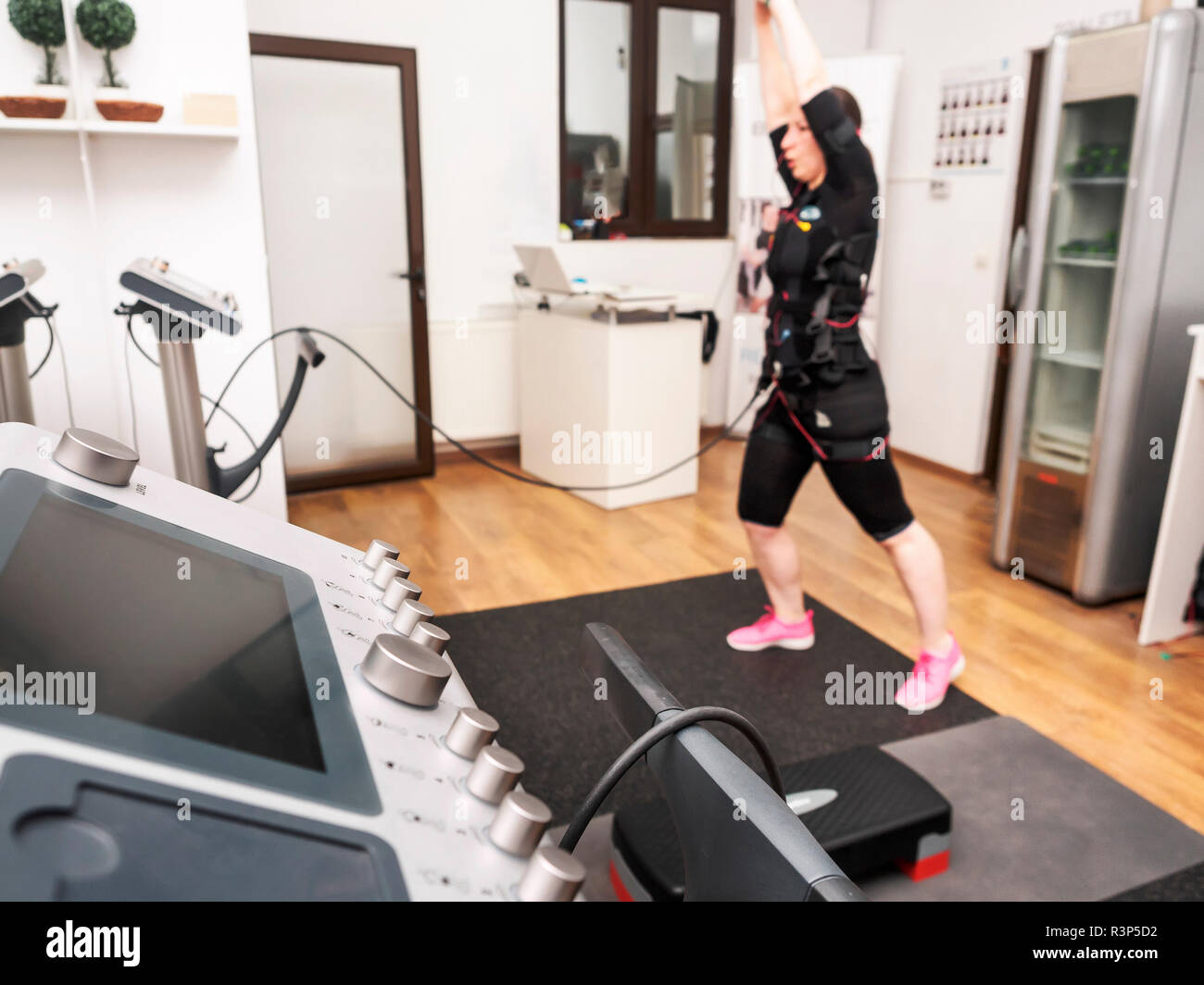 Young woman at the gym by training in a suit with electric impulses. Woman in a suit with electrodes at the gym. Stock Photo