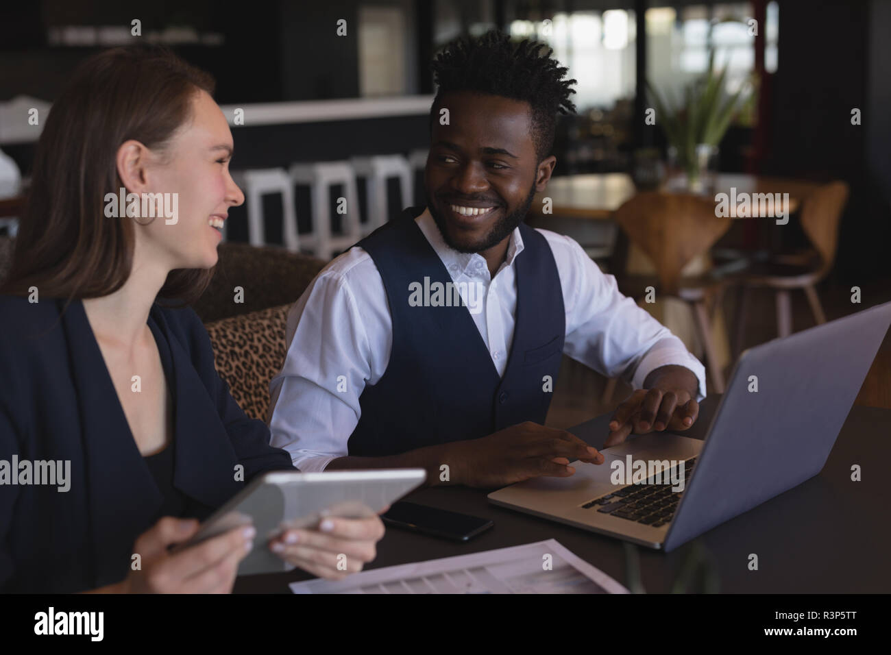 Business colleagues interacting with each other while using digital tablet and laptop Stock Photo