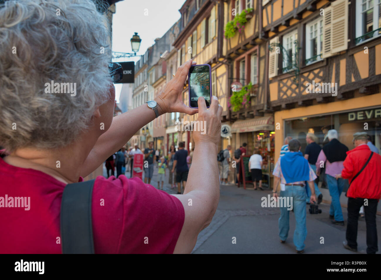 France, Alsace, Colmar. Female tourist in red blouse takes a photograph with her smart phone. (MR) Stock Photo