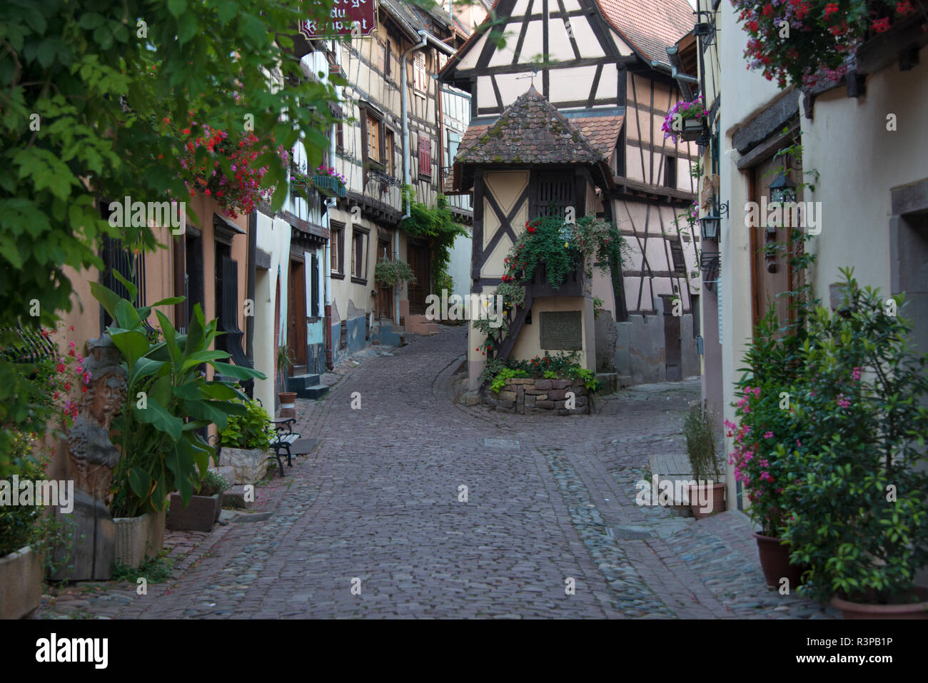 France, Alsace, Eguisheim. A cobblestone street winds between traditional architecture in Eguisheim. Stock Photo
