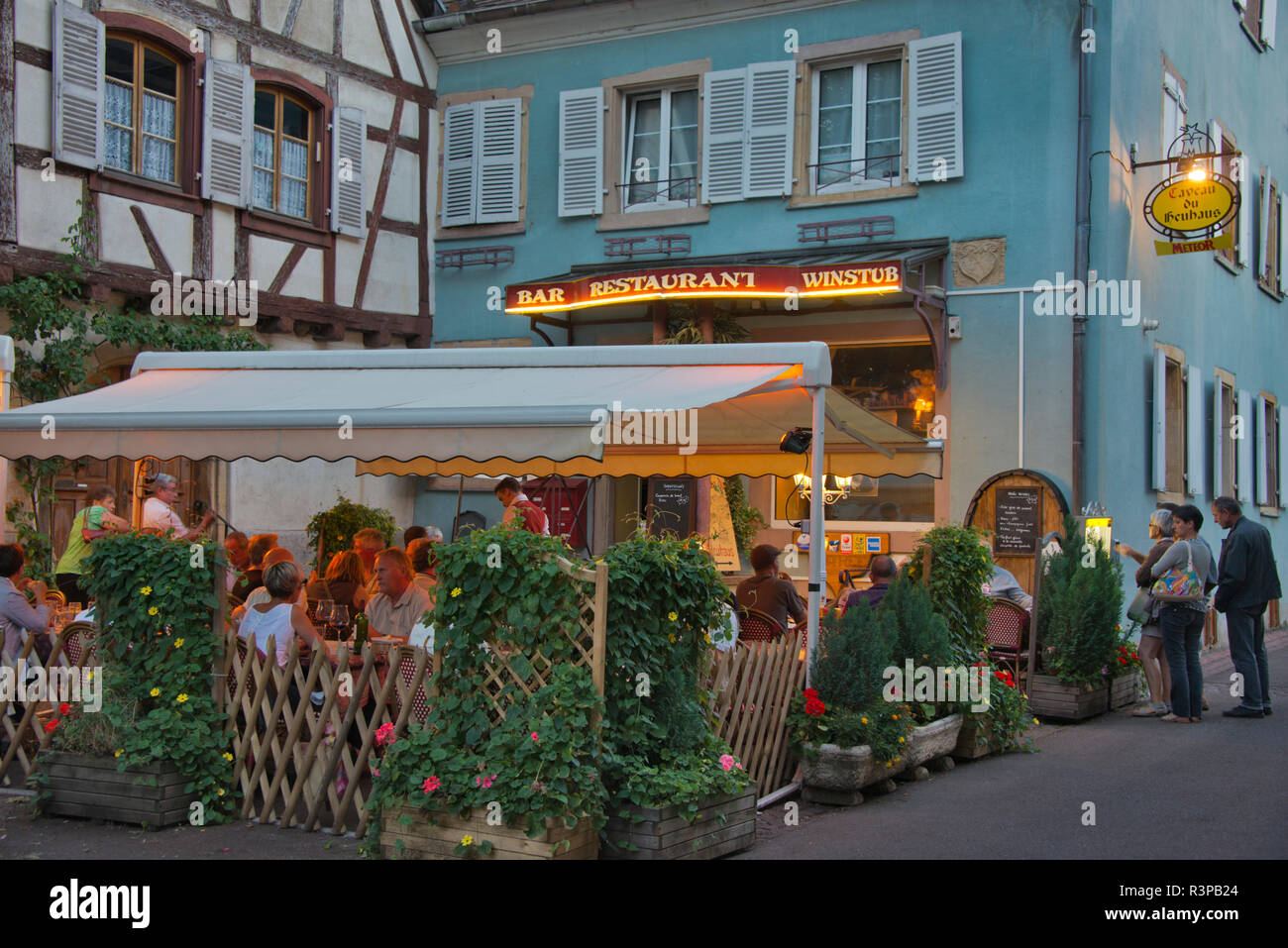 France, Alsace, Eguisheim. People crowd an outdoor restaurant in front of a traditional building in Eguisheim village. Stock Photo