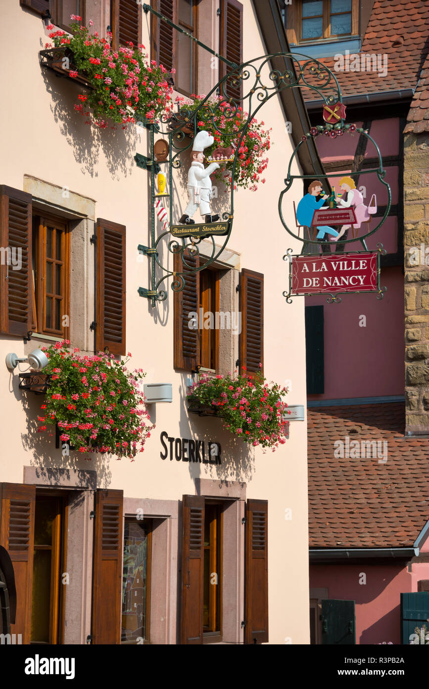 France, Alsace, Eguisheim. Flowers in boxes and sign for a restaurant hang on a traditional building in Eguisheim village. Stock Photo