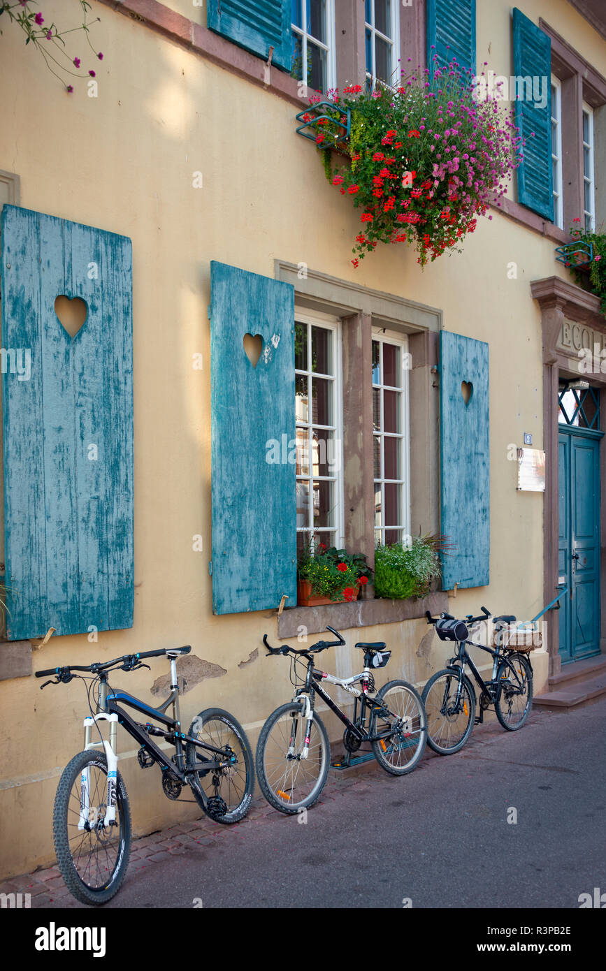 France, Alsace, Eguisheim. Three bicycles leaned against traditional building with blue window shutters. Stock Photo