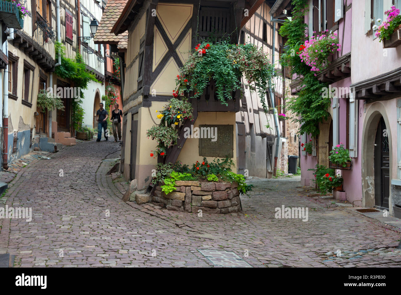 European Union, France, Alsace, Eguisheim village. Tourists walk on cobblestone street winding between traditional architecture of Equisheim village. Stock Photo