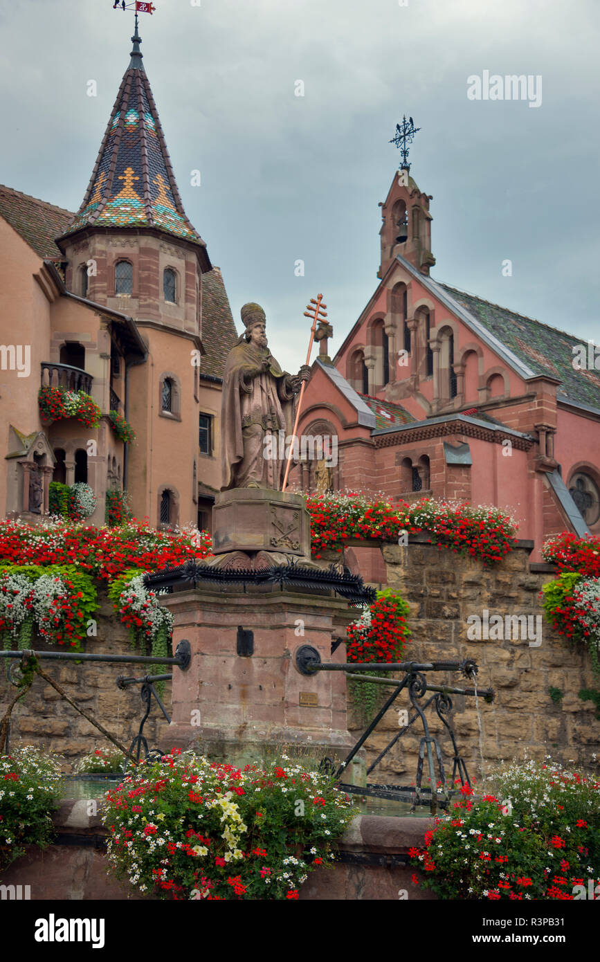 European Union, France, Alsace, Eguisheim village. St Leon church and fountain in Place du Chateau square in medieval Eguisheim village on wine route. Stock Photo