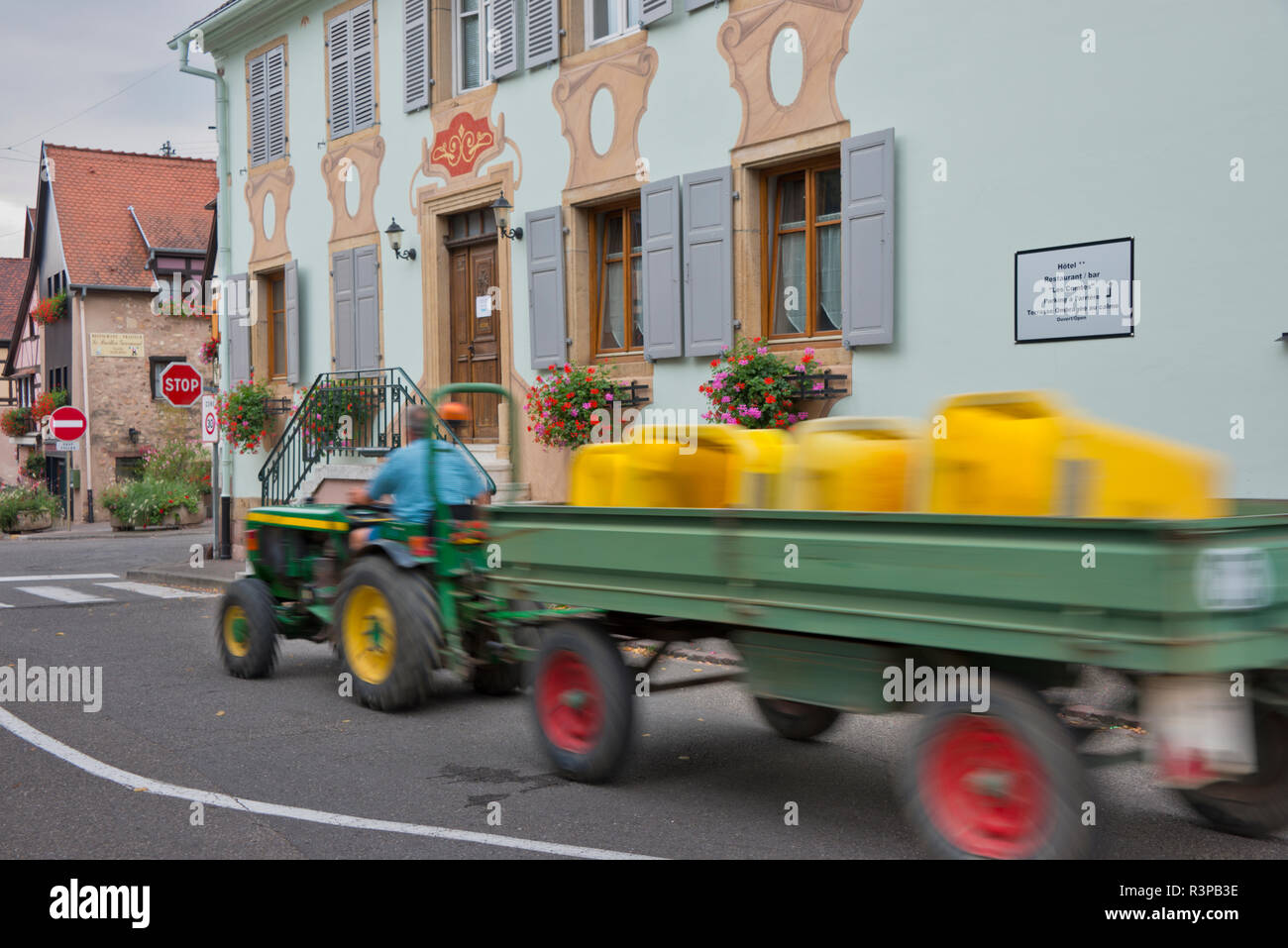 European Union, France, Alsace, Eguisheim village. Tractor pulling a green wagon with yellow containers through traditional Eguisheim village. Stock Photo