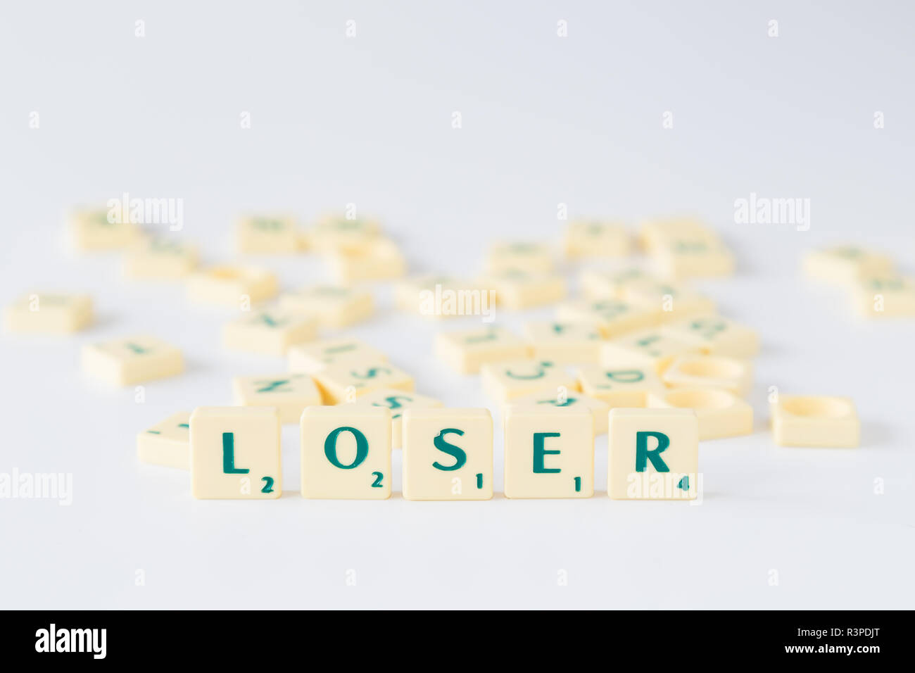 Focus on the word "Loser" made of Scrabble game letter tiles with score value, random tiles mixed up in the background. Shallow depth of field. Stock Photo