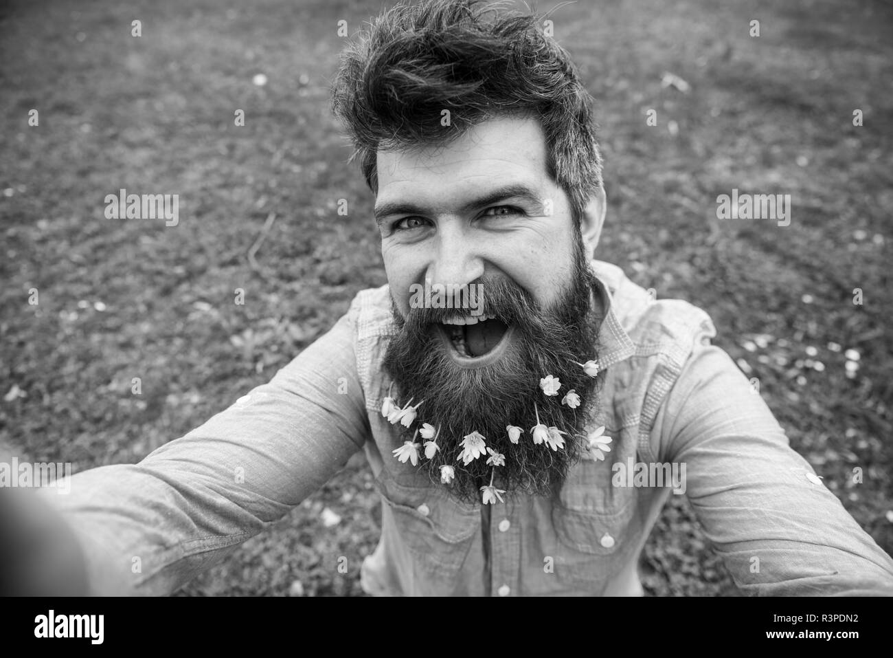 Hipster on happy face taking selfie photo. Man with beard enjoys spring,  green meadow background, defocused. Guy with lesser celandine flowers in  bear Stock Photo - Alamy, image size:1300x957