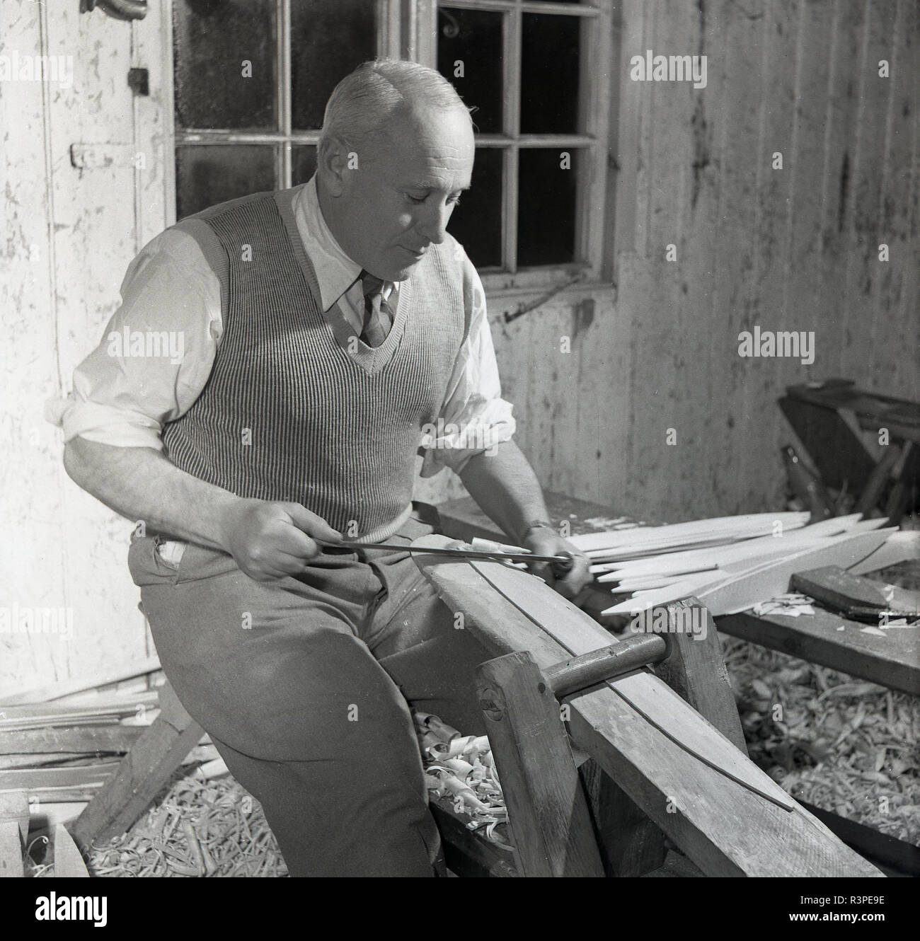 1950s, historical, a male craftsman in his workshop, using a tool to strip willow wood, England, UK. Basket weaving is an old, sacred tradition and was once an important skill in an age when containers were an indispensbale part of life. Stock Photo