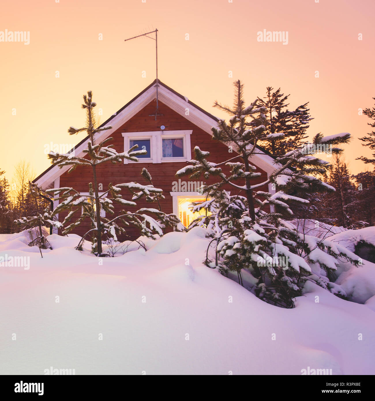 A cozy wooden cabin cottage chalet house covered in snow near ski resort in winter with the lights turn on, evening picture Stock Photo