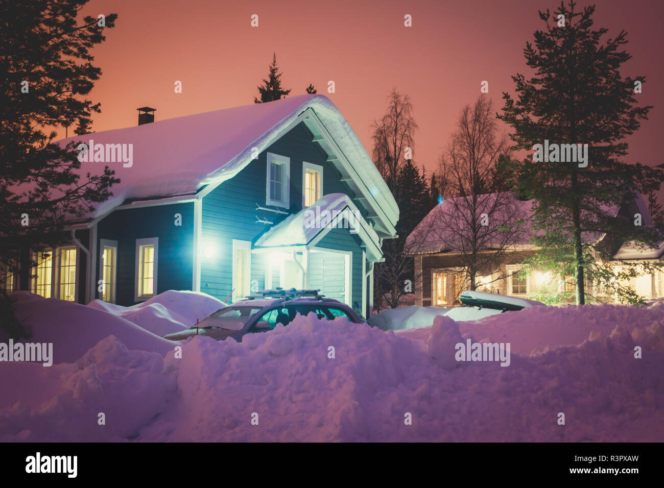 A cozy wooden cabin cottage chalet house covered in snow near ski resort in winter with the lights turn on, evening picture Stock Photo