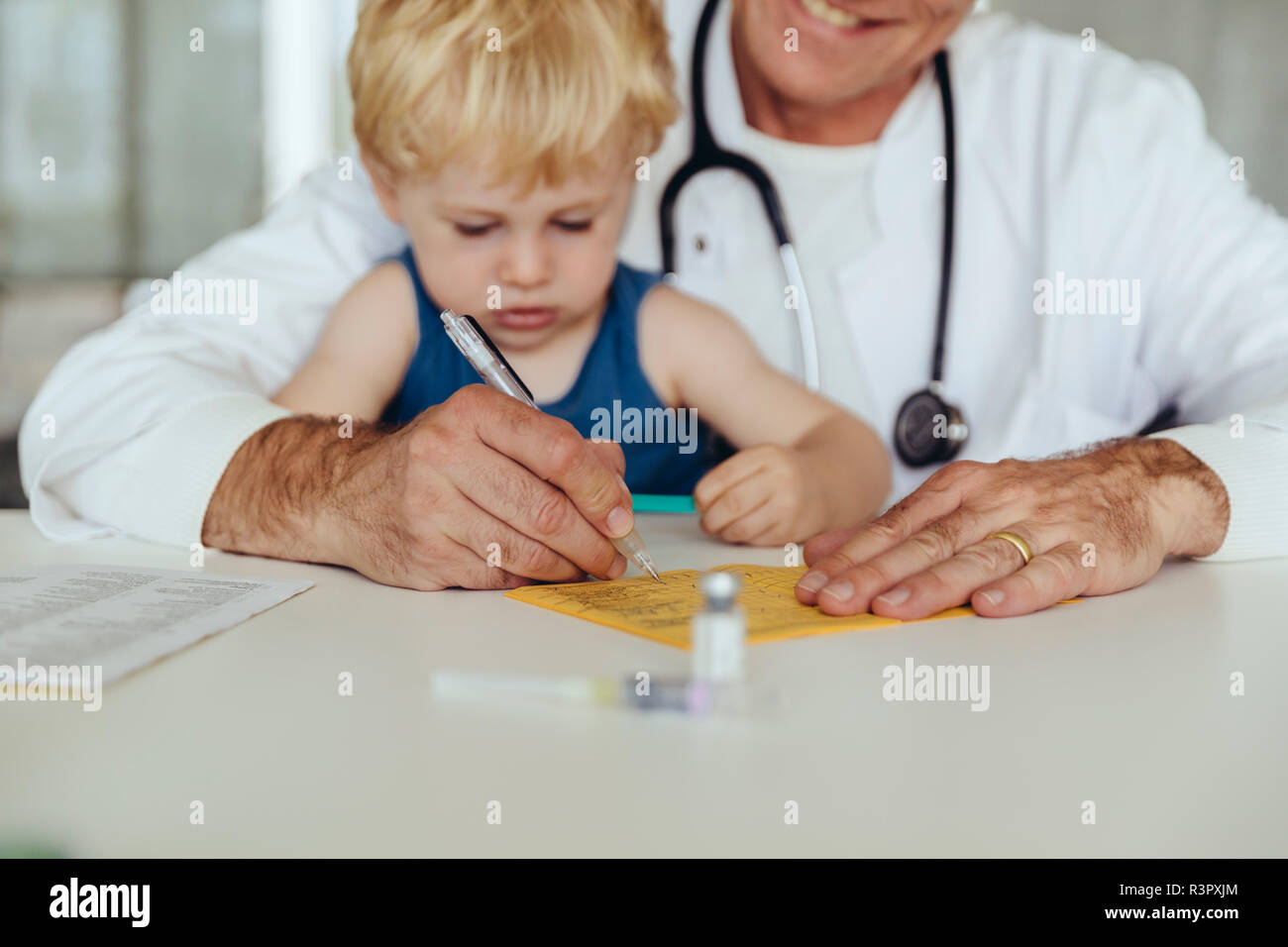 Toddler sitting on doctor's lap, while filling in immunization card Stock Photo