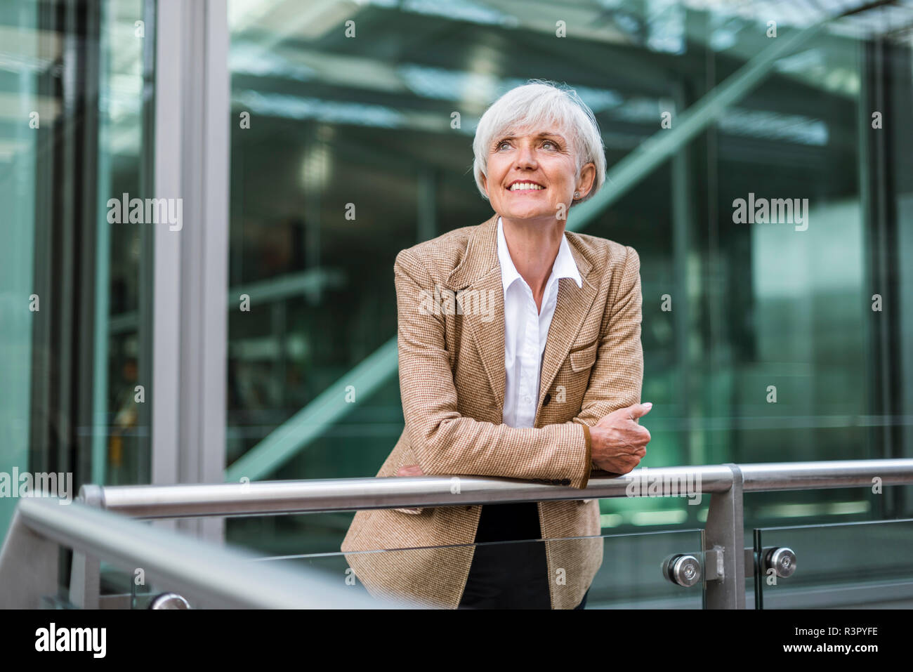 Portrait of smiling senior businesswoman leaning on railing in the city looking up Stock Photo