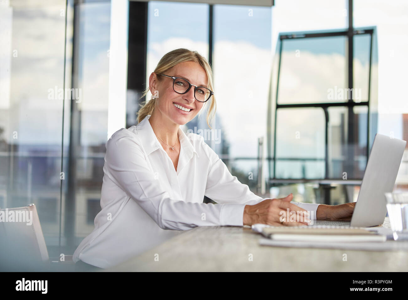 Businesswoman sitting at desk, using laptop, smiling friendly Stock Photo