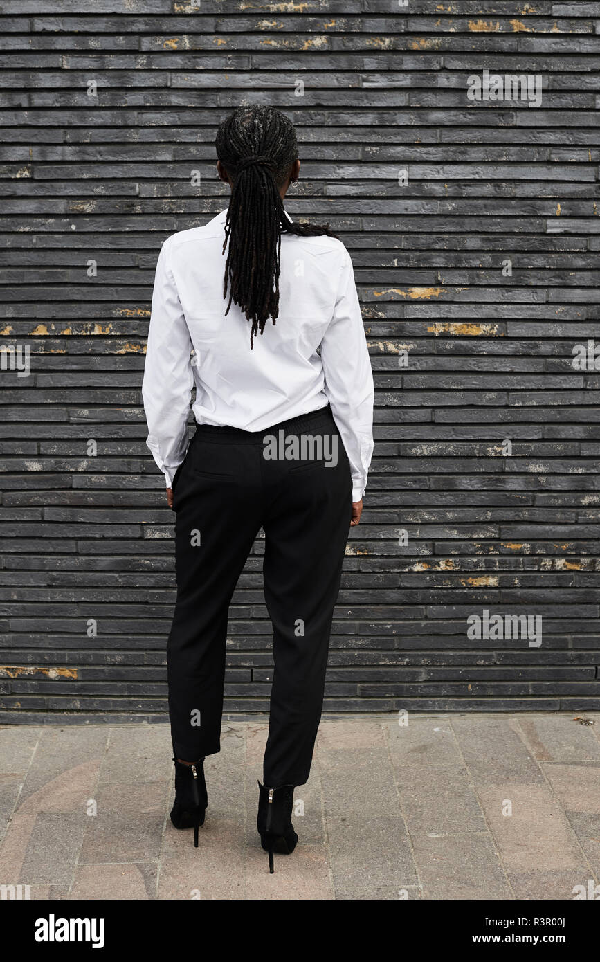 Back view of businesswoman with dreadlocks wearing white shirt and black trousers Stock Photo