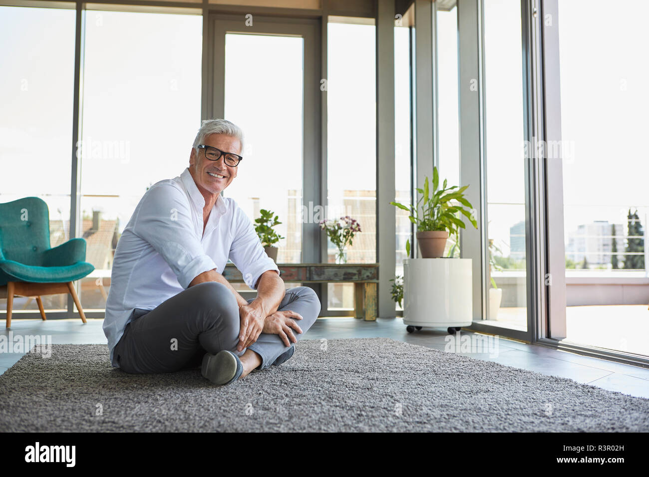 Smiling mature man relaxing sitting on carpet at home Stock Photo