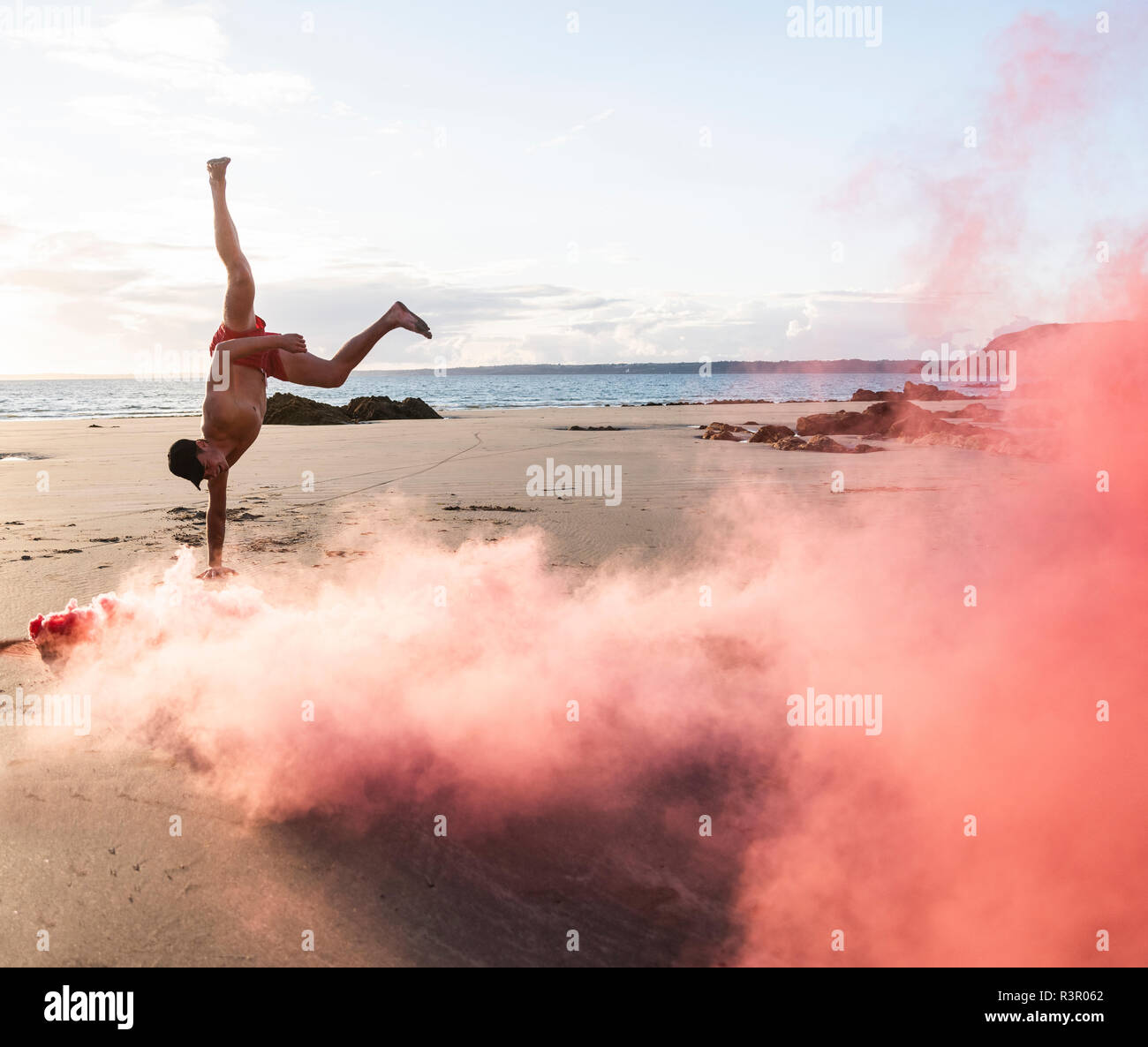 Man doing movement training at the beach with red smoke Stock Photo