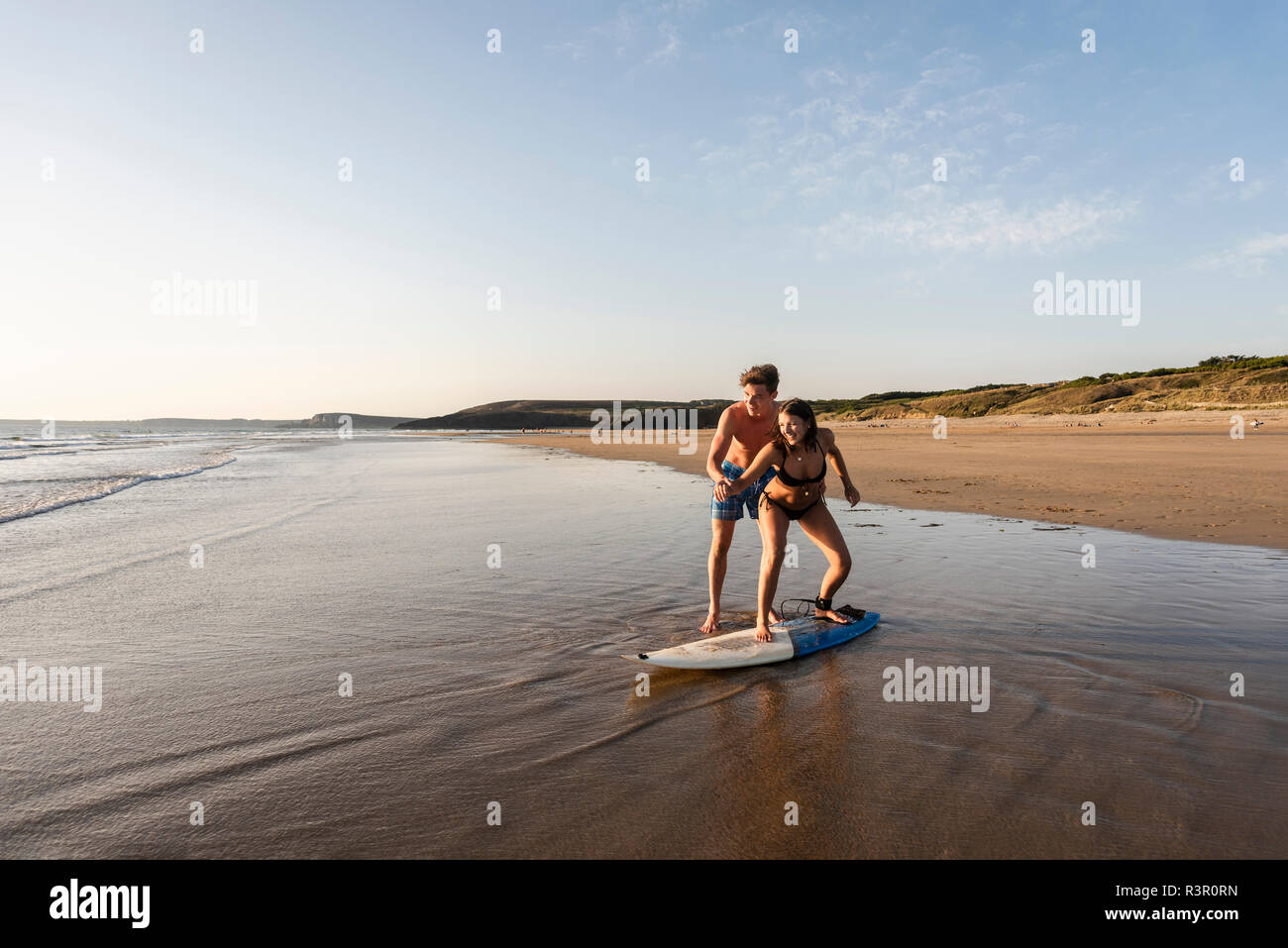 Young man showing young woman how to surf on the beach Stock Photo