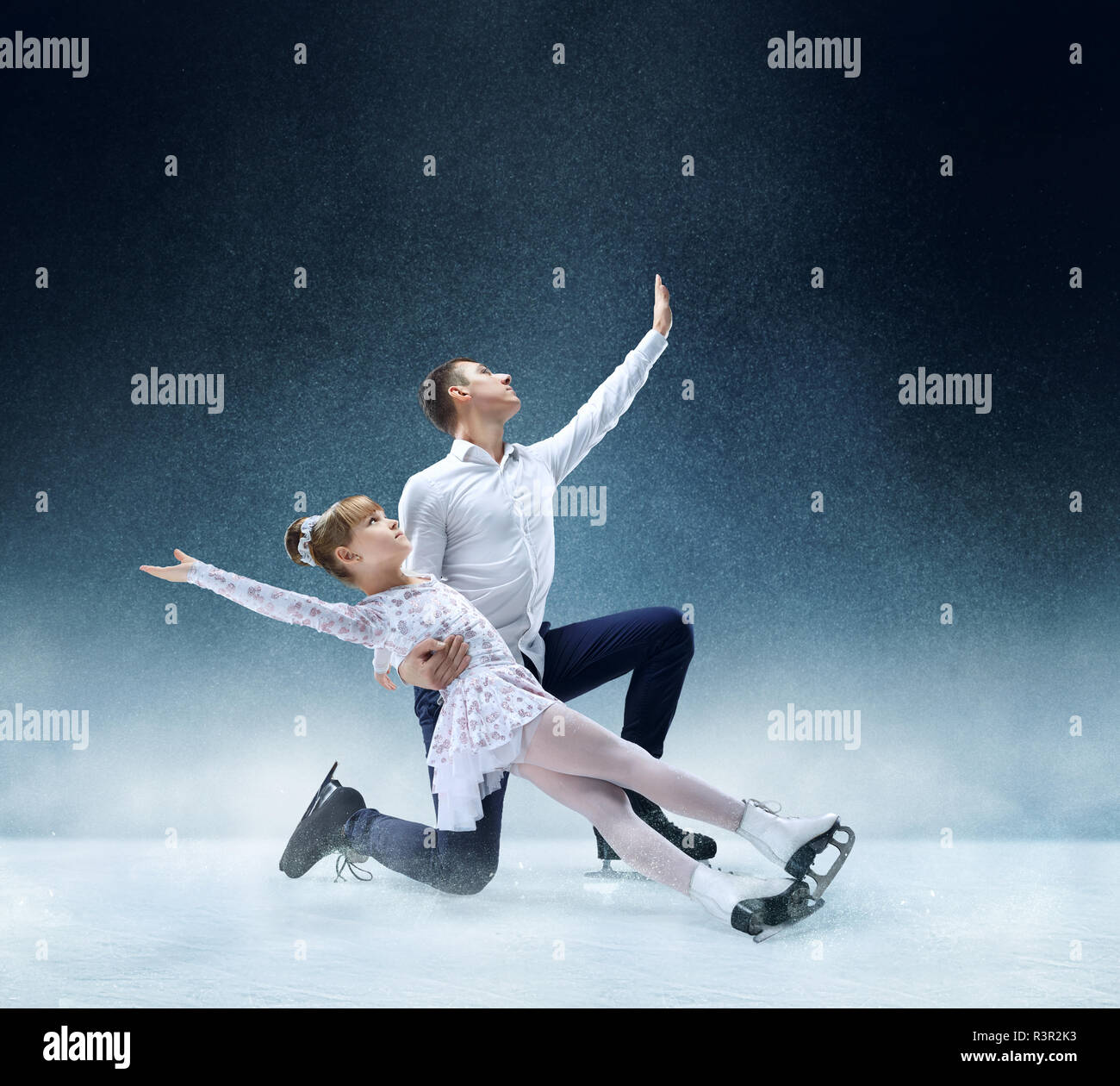 Little girl figure skating withe male trainer at the indoor ice arena