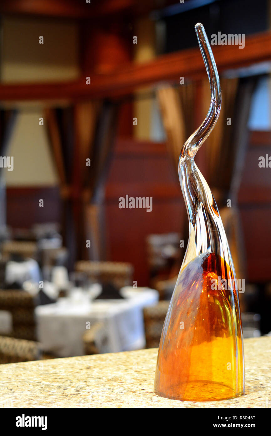 A twisted, tall glass art piece in the foreground of tables at a fancy restaurant, with a shallow depth of field Stock Photo