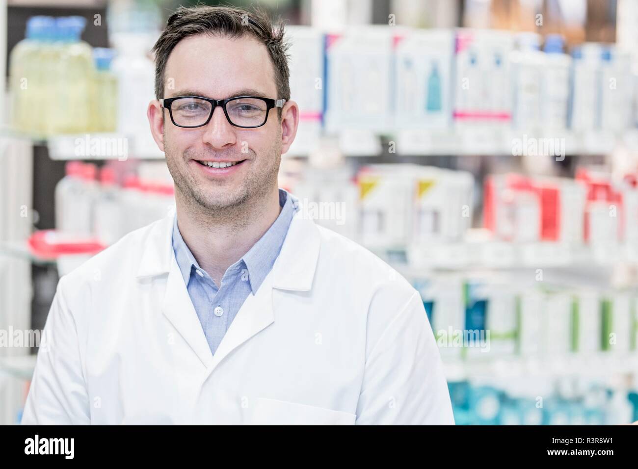 Portrait of young male pharmacist standing in pharmacy. Stock Photo
