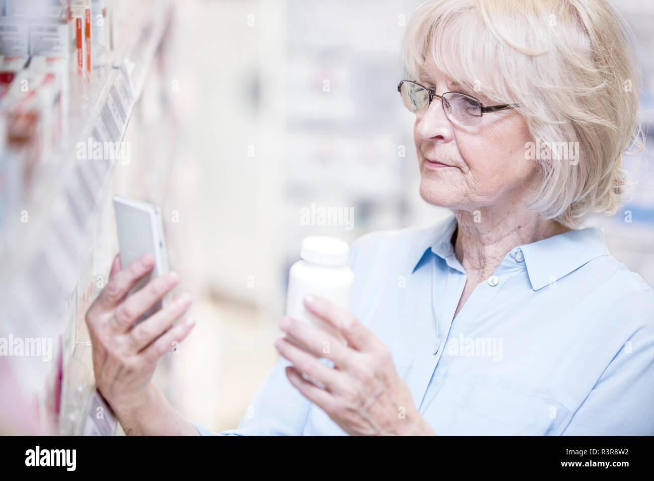 Senior woman checking medicine on mobile phone in pharmacy. Stock Photo