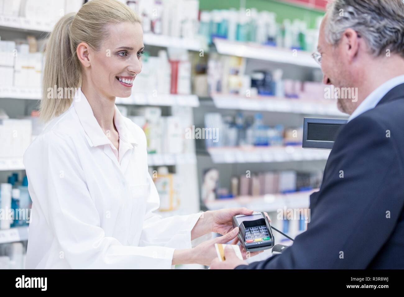 Mature man paying female pharmacist in pharmacy. Stock Photo