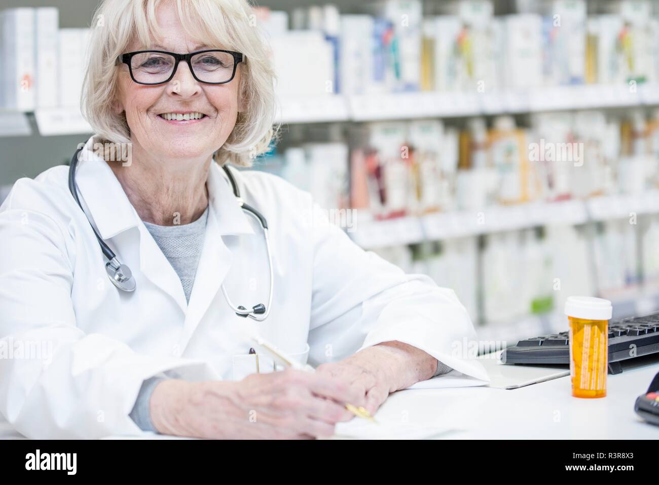 Portrait of smiling senior pharmacist writing on prescription. Stock Photo