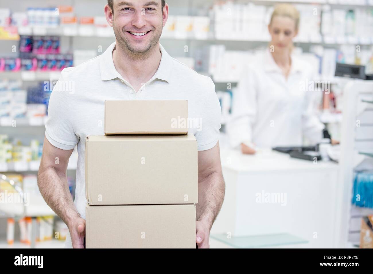 Courier carrying boxes in pharmacy with pharmacist in background. Stock Photo