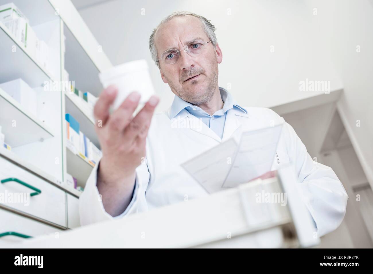 Male pharmacist reading label on pill bottle while looking for medicine in drawer cabinet in pharmacy. Stock Photo