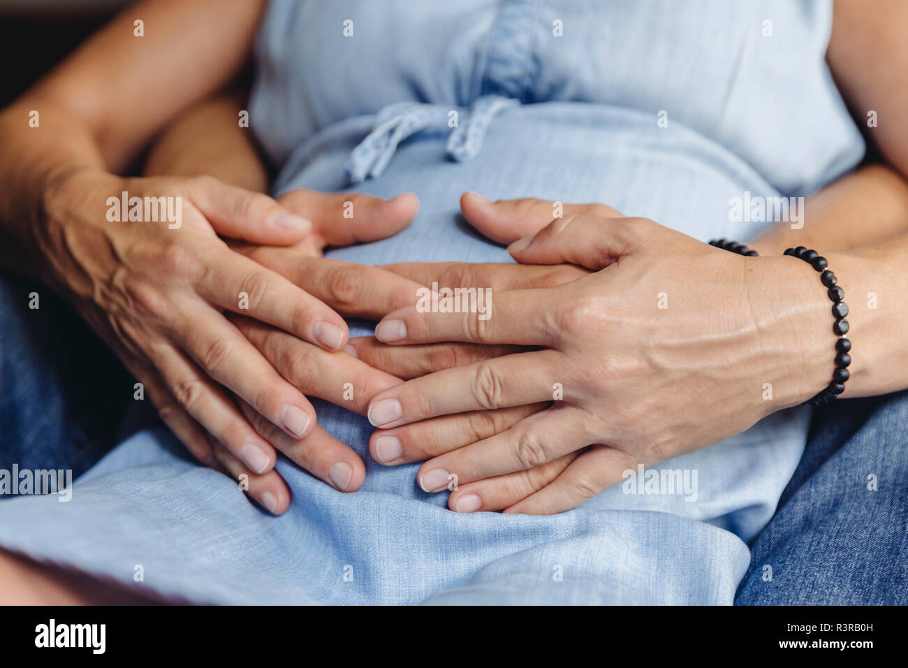 Hands of mature man and his pregnant mature wife touching her belly Stock Photo