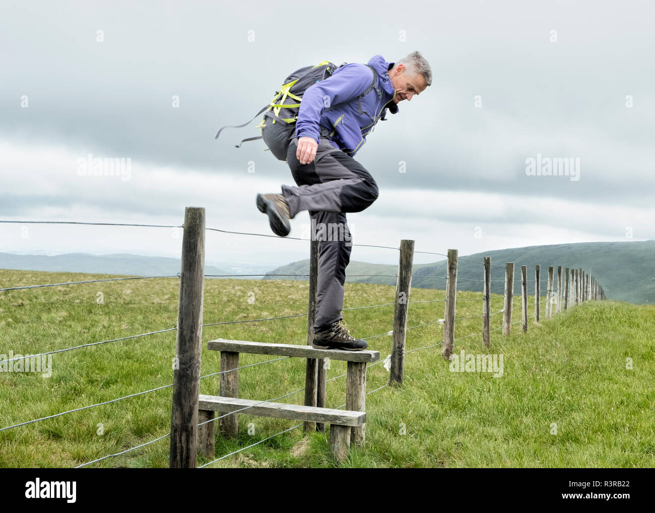 UK, Lake District, Longsleddale valley, mature man with backpack crossing pasture fence Stock Photo
