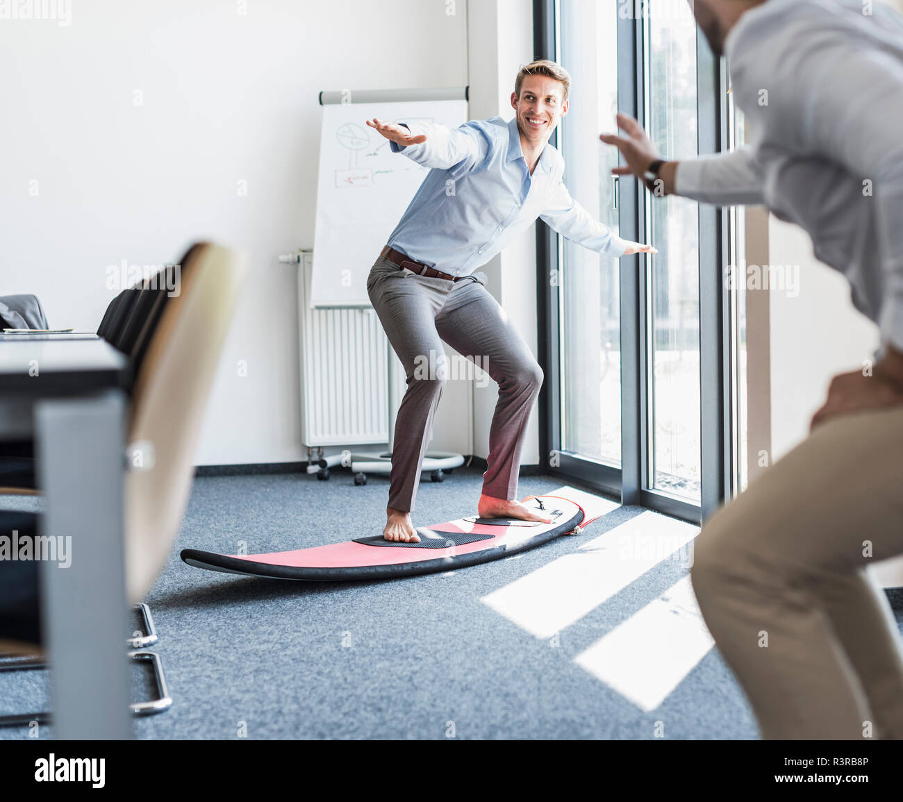Two playful colleagues with surfboard in office Stock Photo