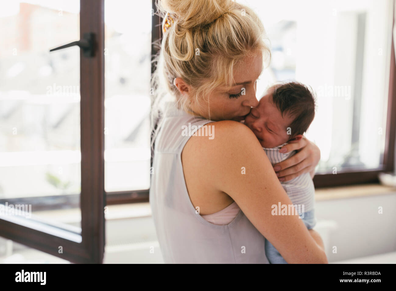 Mother holding her crying baby close to her shoulder at home Stock Photo