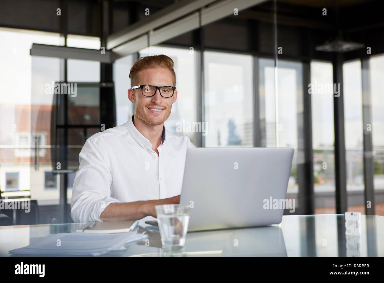 Portrait of smiling businessman using laptop on desk in office Stock Photo