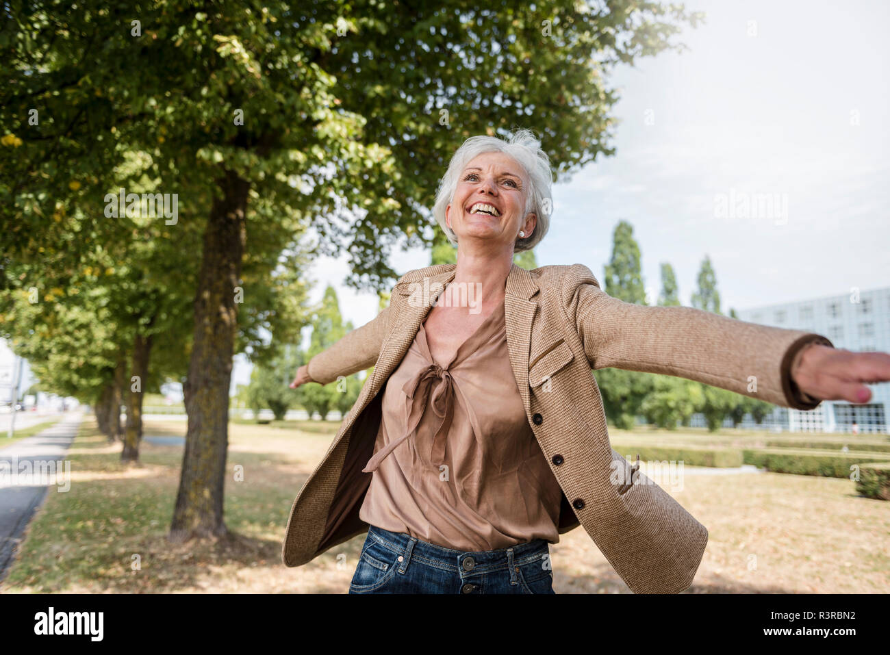 Happy senior woman with outstretched arms in a park Stock Photo