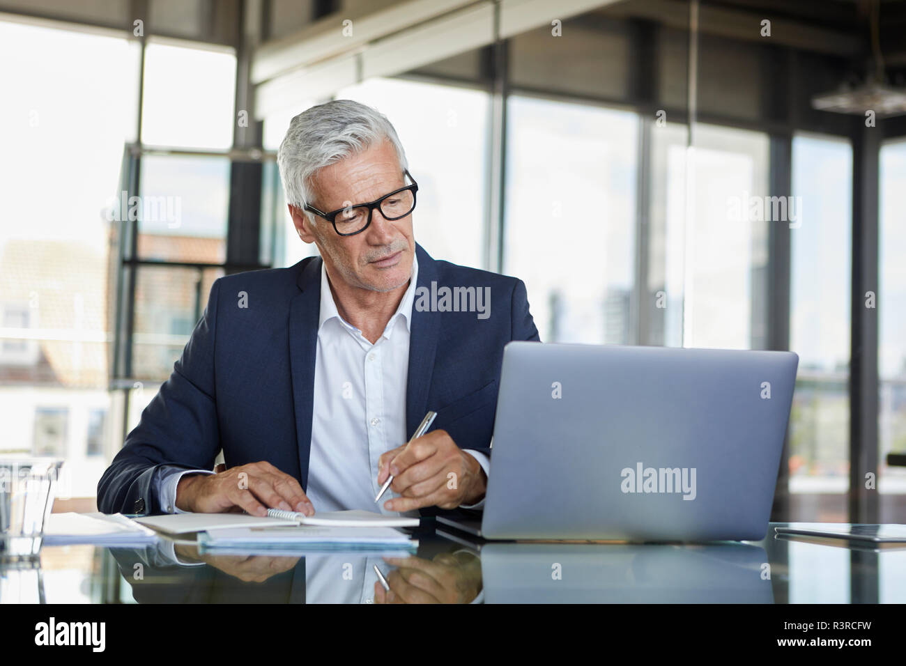 Businessman working at laptop, taking notes in notebook Stock Photo
