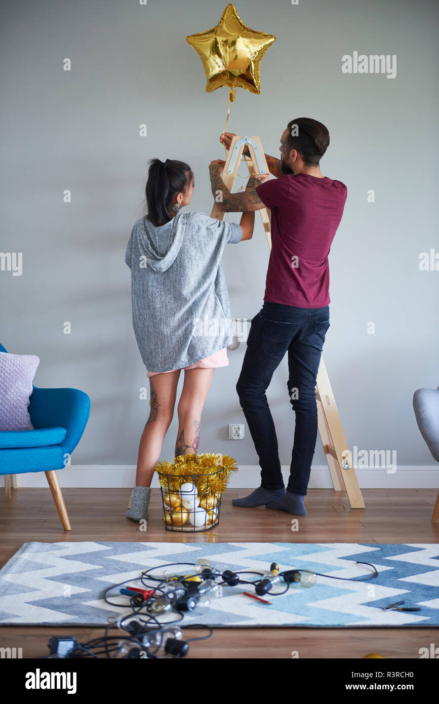Modern couple decorating the home at Christmas time using ladder as Christmas tree Stock Photo