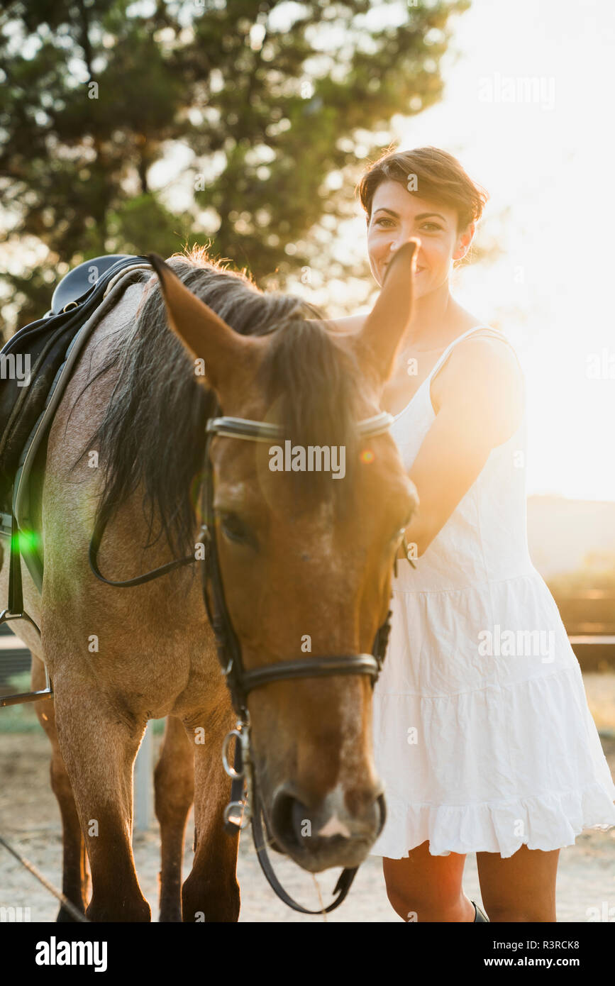 Portrait of smiling woman standing besides riding horse at backlight Stock Photo