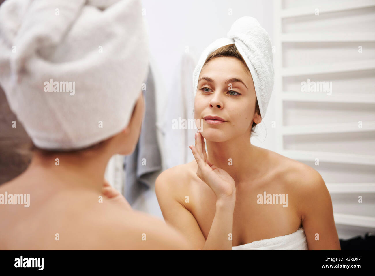 Mirror image of young woman examining her face in the bathroom Stock Photo