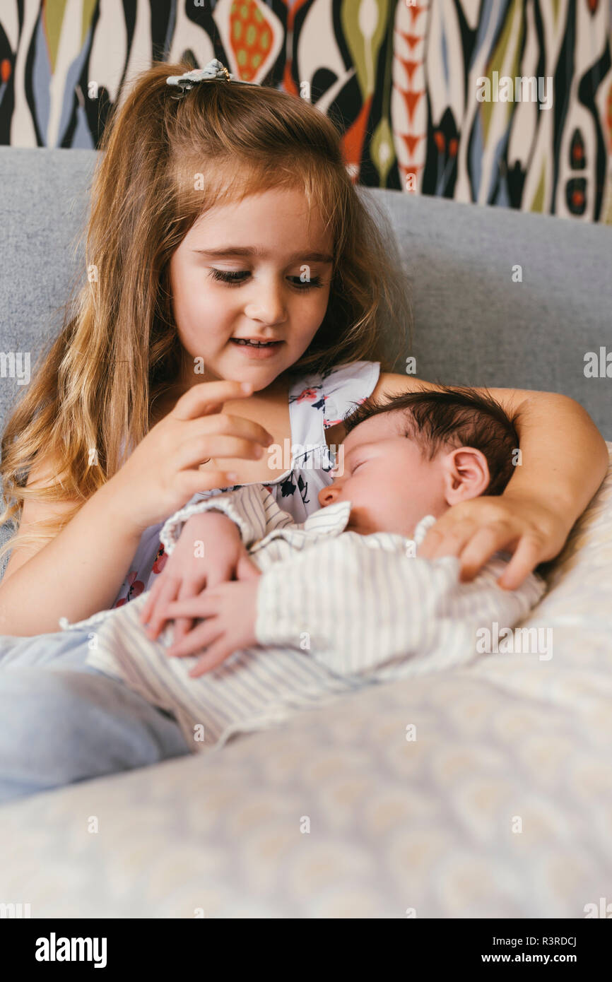Girl sitting on couch looking at newborn baby brother Stock Photo